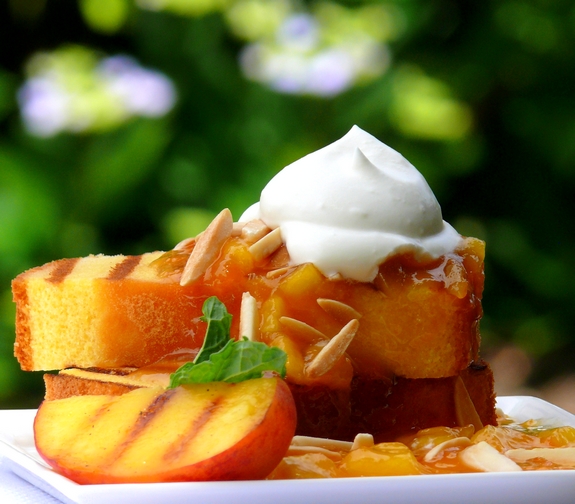 Grilled peaches, grilled pound cake with peach coulis and chantilly cream on a plate.