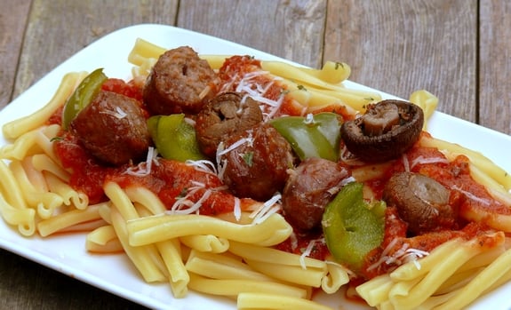 Sausage kabobs sitting on top of pasta.