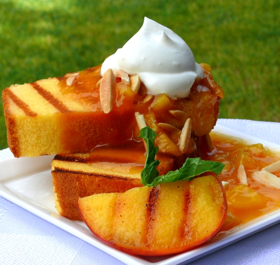 Grilled pound cake, warm peach coulis with a chantilly cream sauce on a white plate with mint garnish.