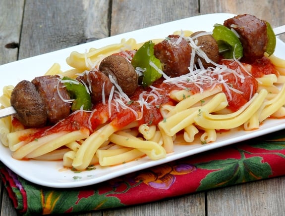 Sausage kabob sitting on top of pasta with marinara.