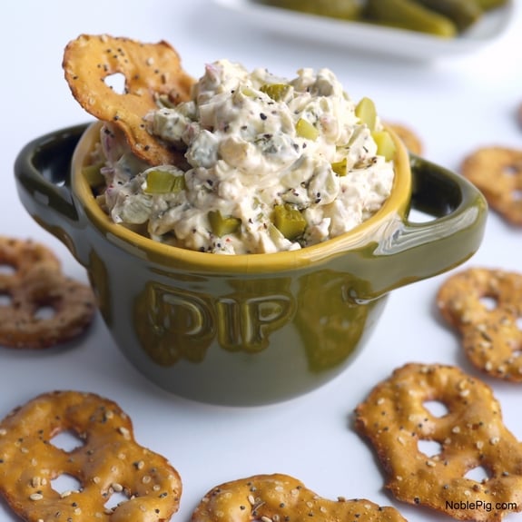 Dill Pickle Dip in a green bowl surrounded by pretzels and a pretzel in the dip.