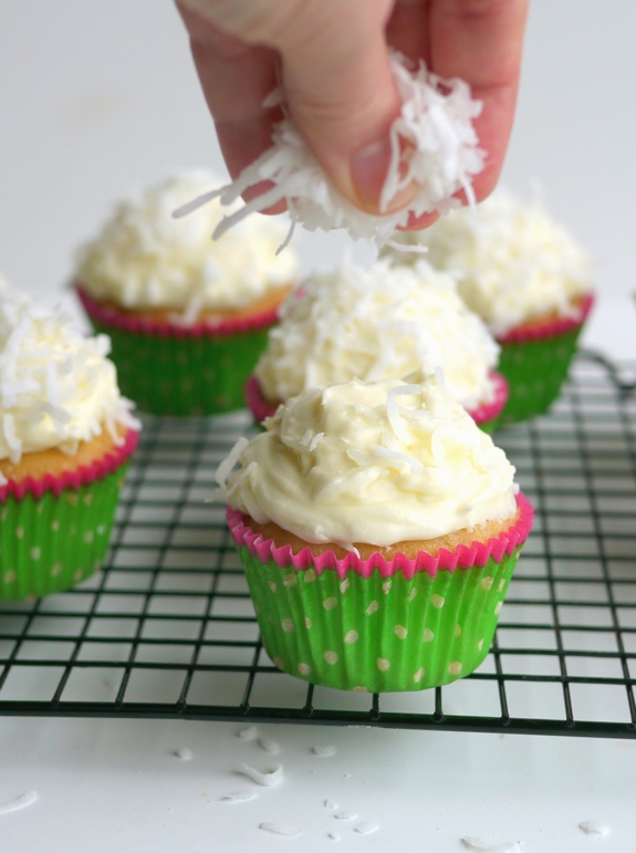 Coconut Overload Cupcakes that are being sprinkled with coconut. 