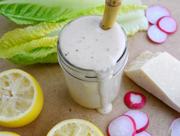 Creamy Parmesan Salad Dressing in a jar surrounded by lemons, radishes, lettuce and cheese.