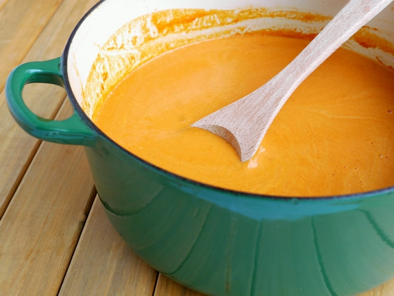 Creamy Tomato Chipotle Soup in a green pot with a wooden spoon.