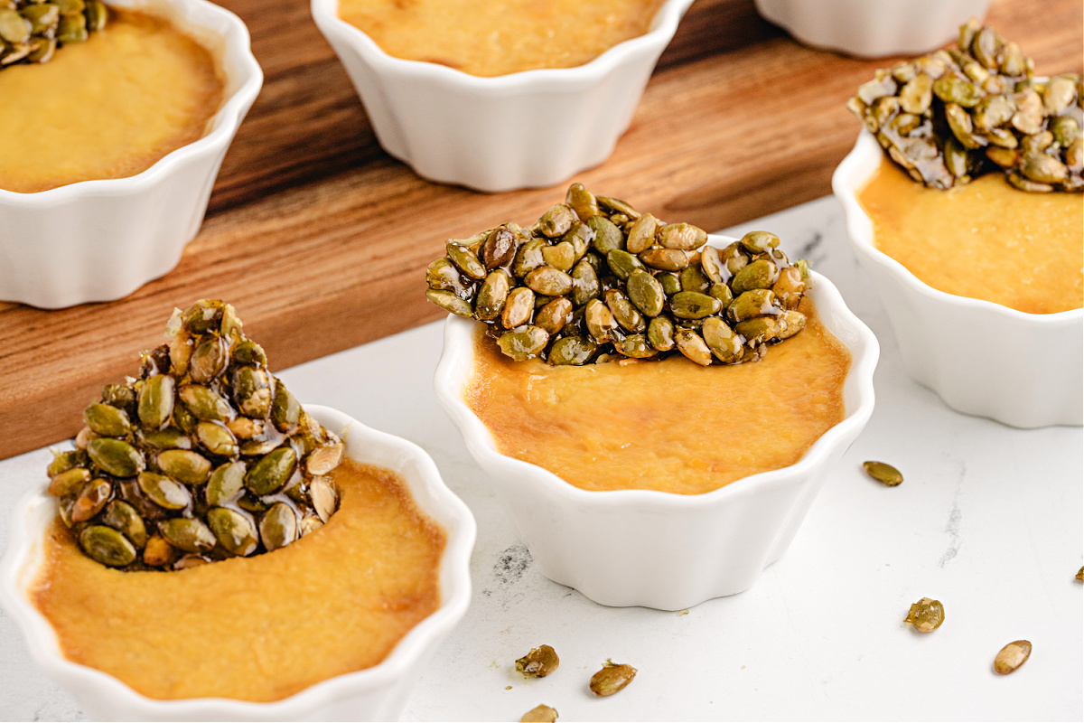 Pumpkin Chai Pots de Cr&egrave;me by Noble Pig arranged in white ramekins with crisp pepita brittle for a grown-up fall dessert.