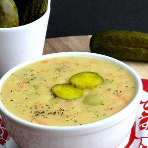 Dill pickle soup in a bowl sitting on a red and white plate.