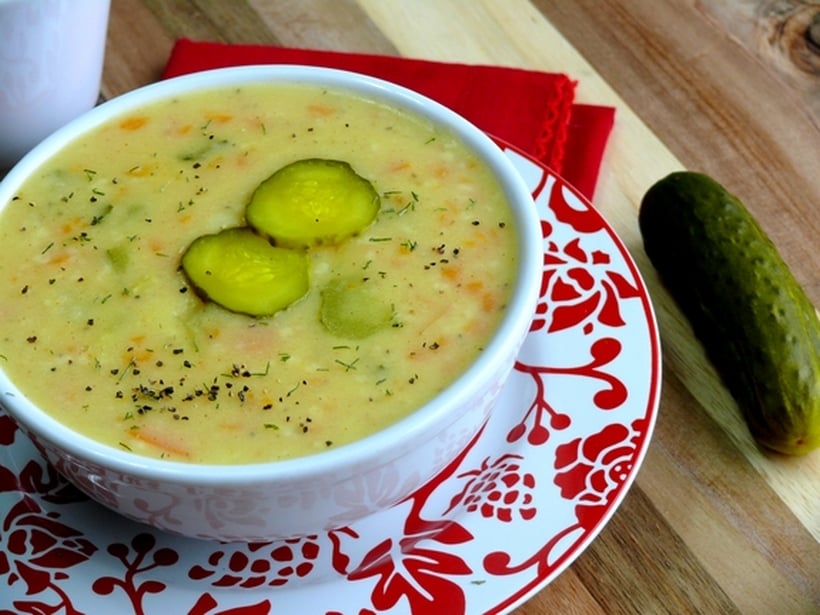 Dill pickle soup in a white bowl sitting on a red and white plate.