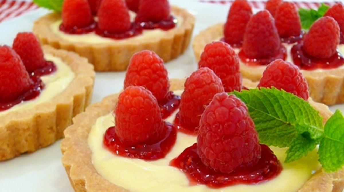 raspberry lemon tartlets close up Homemade raspberry lemon tartlets topped with fresh raspberries and raspberry jam on a white serving platter.