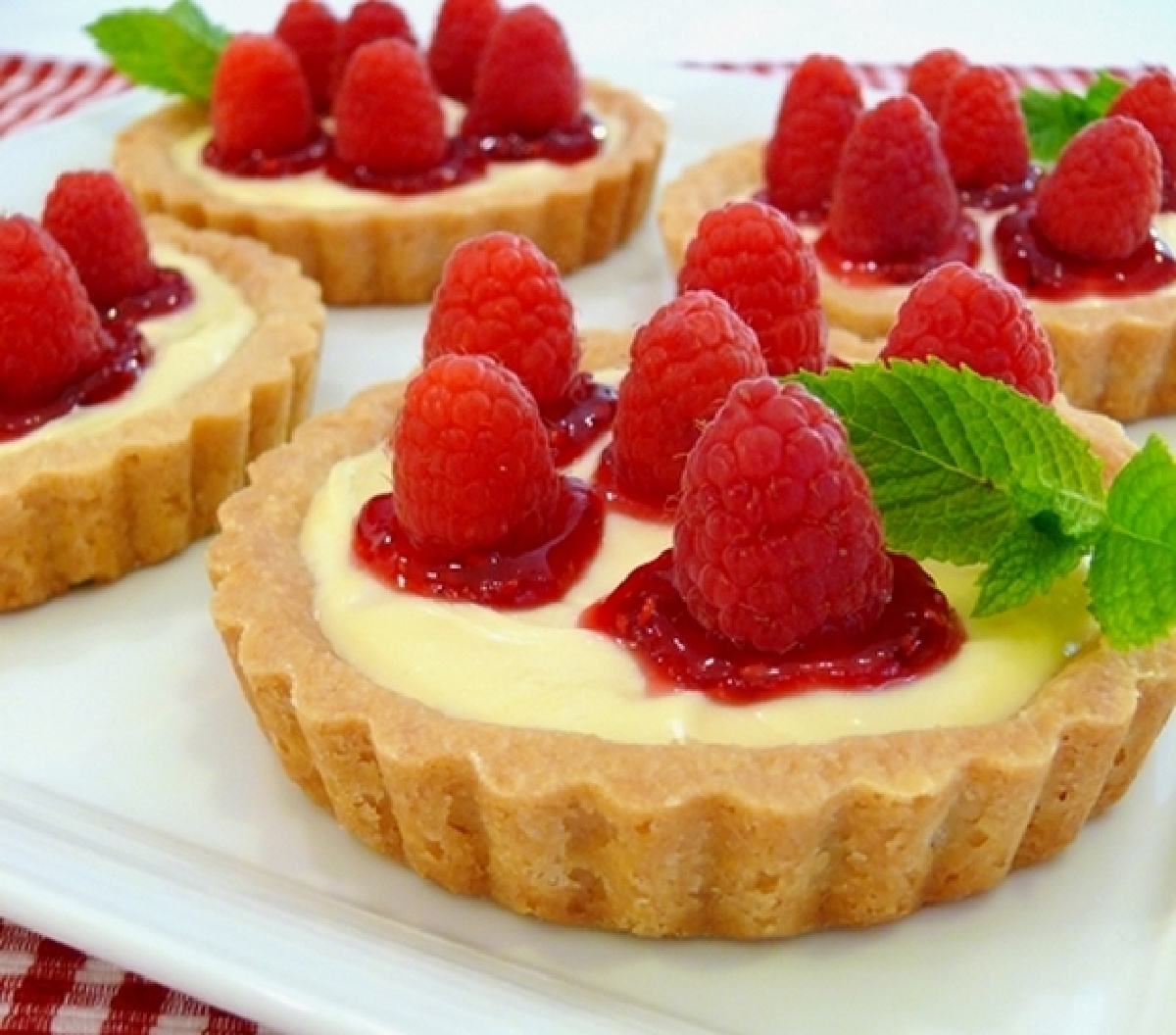 Fresh raspberries sit on raspberry jam and creamy lemon filling inside crisp shortbread tartlet shells. Close-up of raspberry lemon tartlets with lemon curd filling, raspberry jam, fresh raspberries, and a buttery shortbread crust.