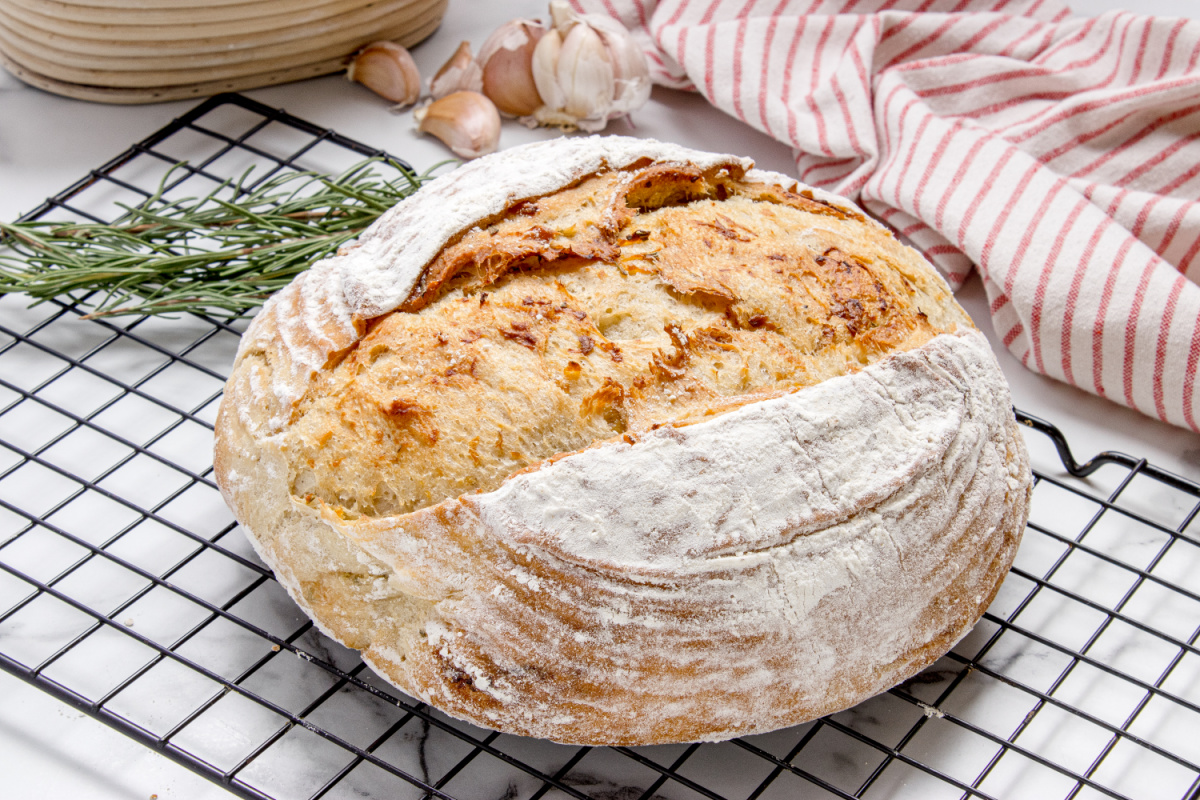 Crackly roasted garlic rosemary artisan bread loaf Roasted garlic rosemary artisan bread cooling on a wire rack with a crisp crackly crust
