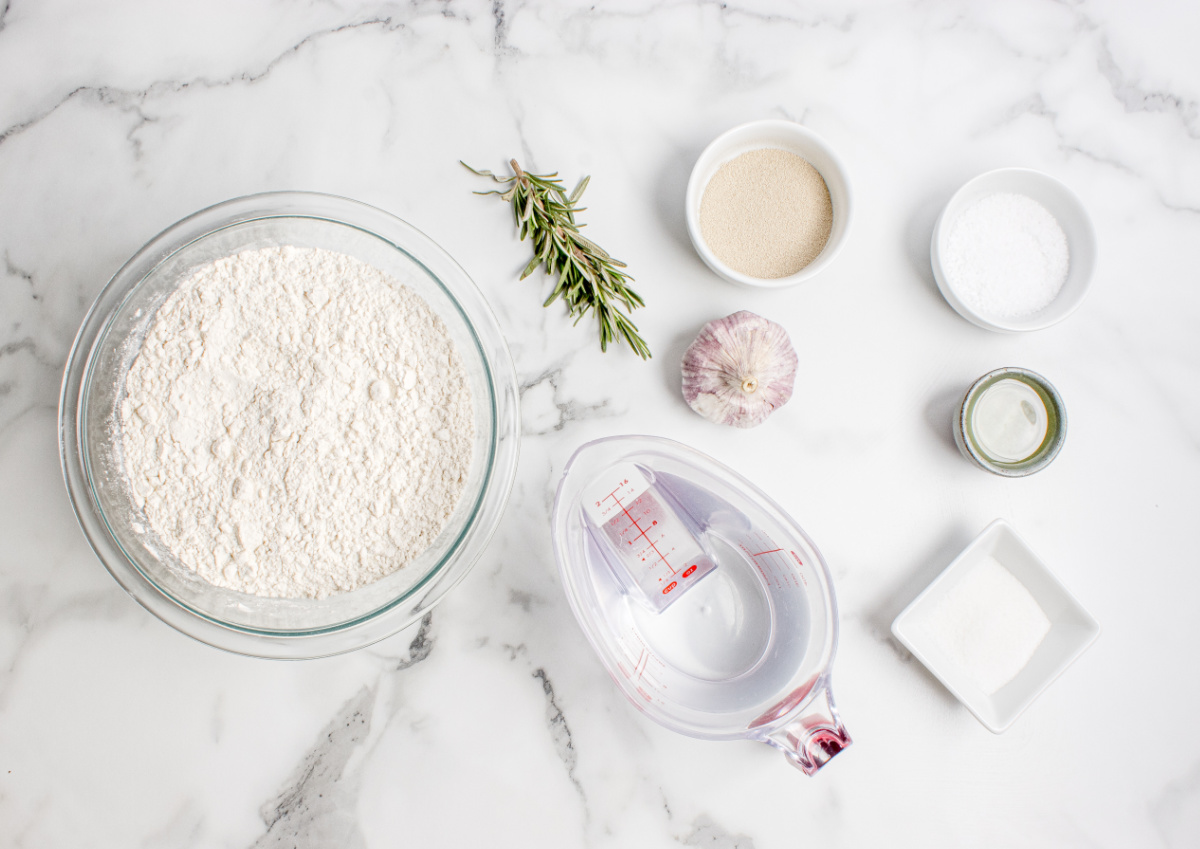 Roasted garlic rosemary artisan bread ingredients Ingredients for roasted garlic rosemary artisan bread including flour, yeast, rosemary, garlic, olive oil, and water