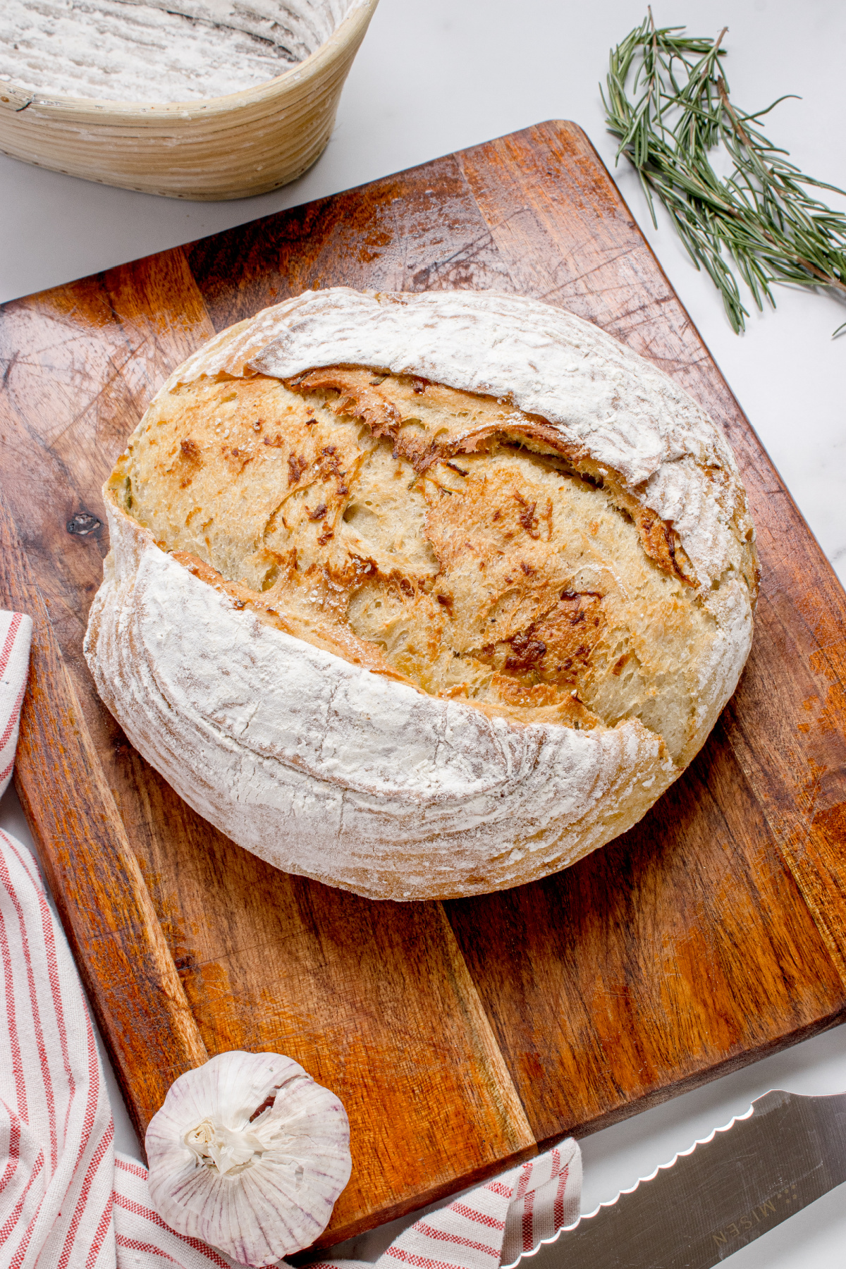 Roasted garlic rosemary artisan bread baked in a Dutch oven with a crackly golden crust on a wooden board
