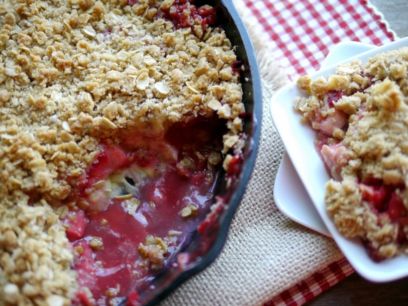 Strawberry-Banana Crumble in a cast iron pan with a scoop missing and served on a plate.