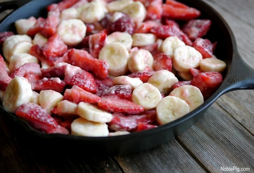 Sliced strawberries and banana in a cast iron pan.