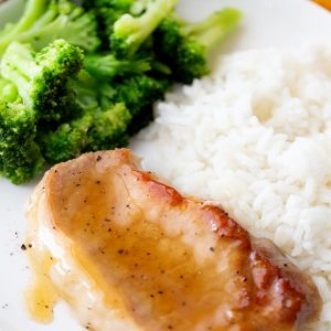 Glazed Pork chop sitting on a plate with rice and broccoli.