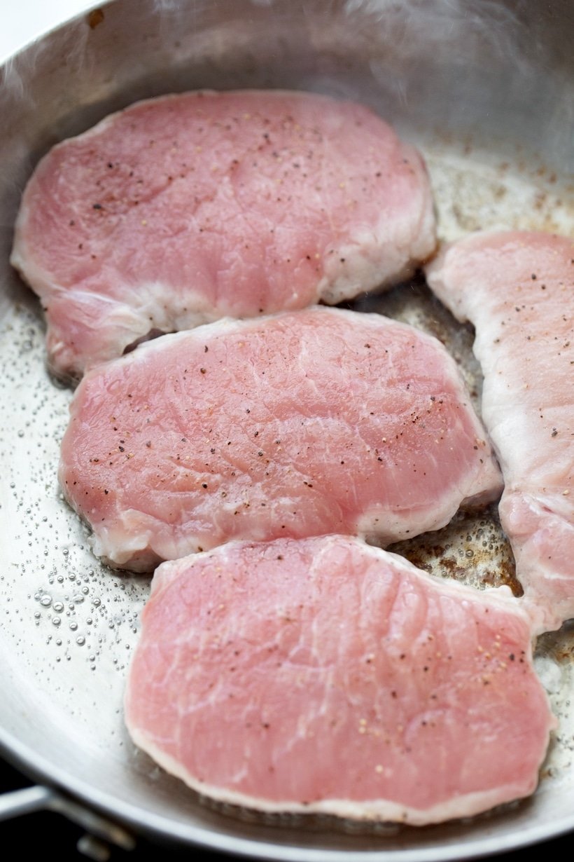 Raw pork chops in a skillet.