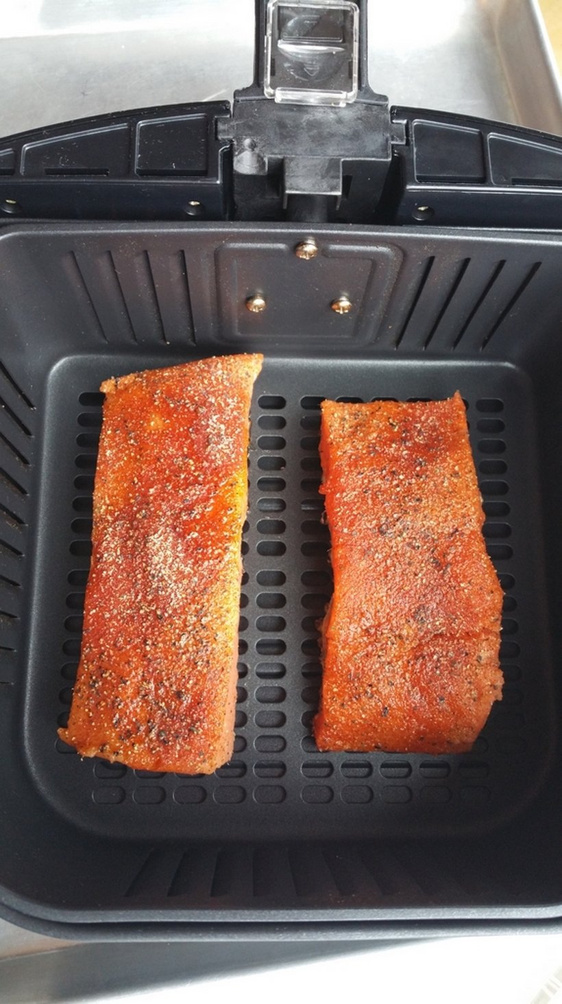 Two pieces of raw salmon in the basket of an air fryer.