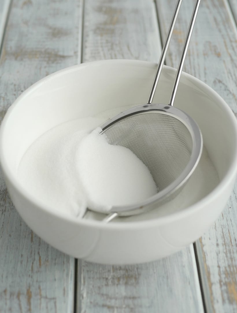 Bowl of sugar with a sifter inside.