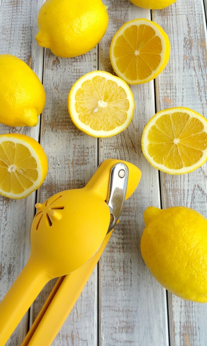 Yellow citrus squeezer with whole and sliced lemons.