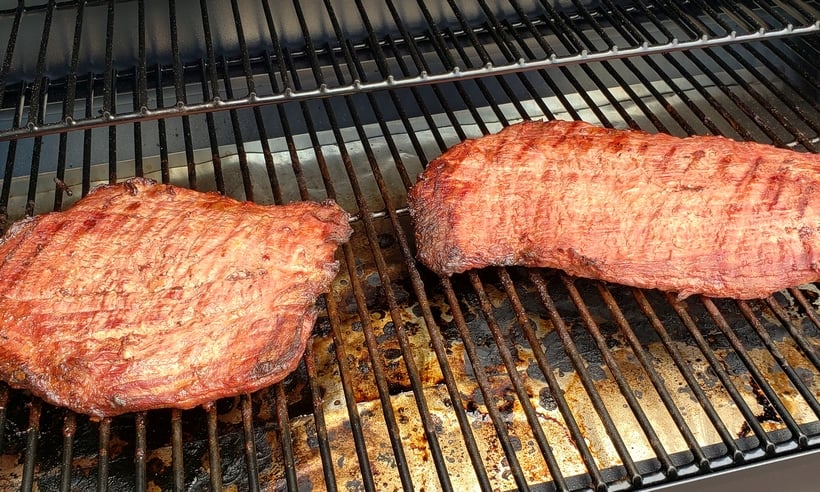 Two flank steaks sitting on a grill plate.