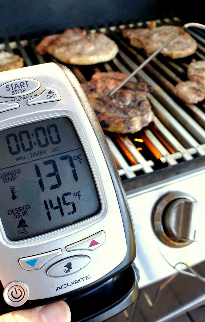 Pork chops cooking on a grill with a digital meat thermometer taking their temperature.