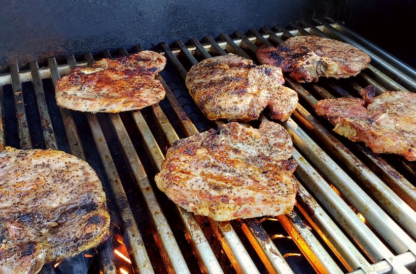 Pork chops cooking on a grill.