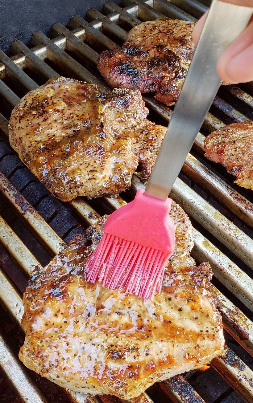 Pork chops on a grill being basted with a brush.