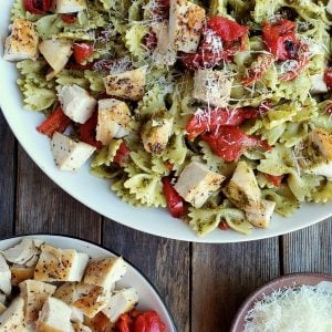 Chicken pesto pasta in a white bowl with grated Parmesan and a bowl of chicken and red peppers.