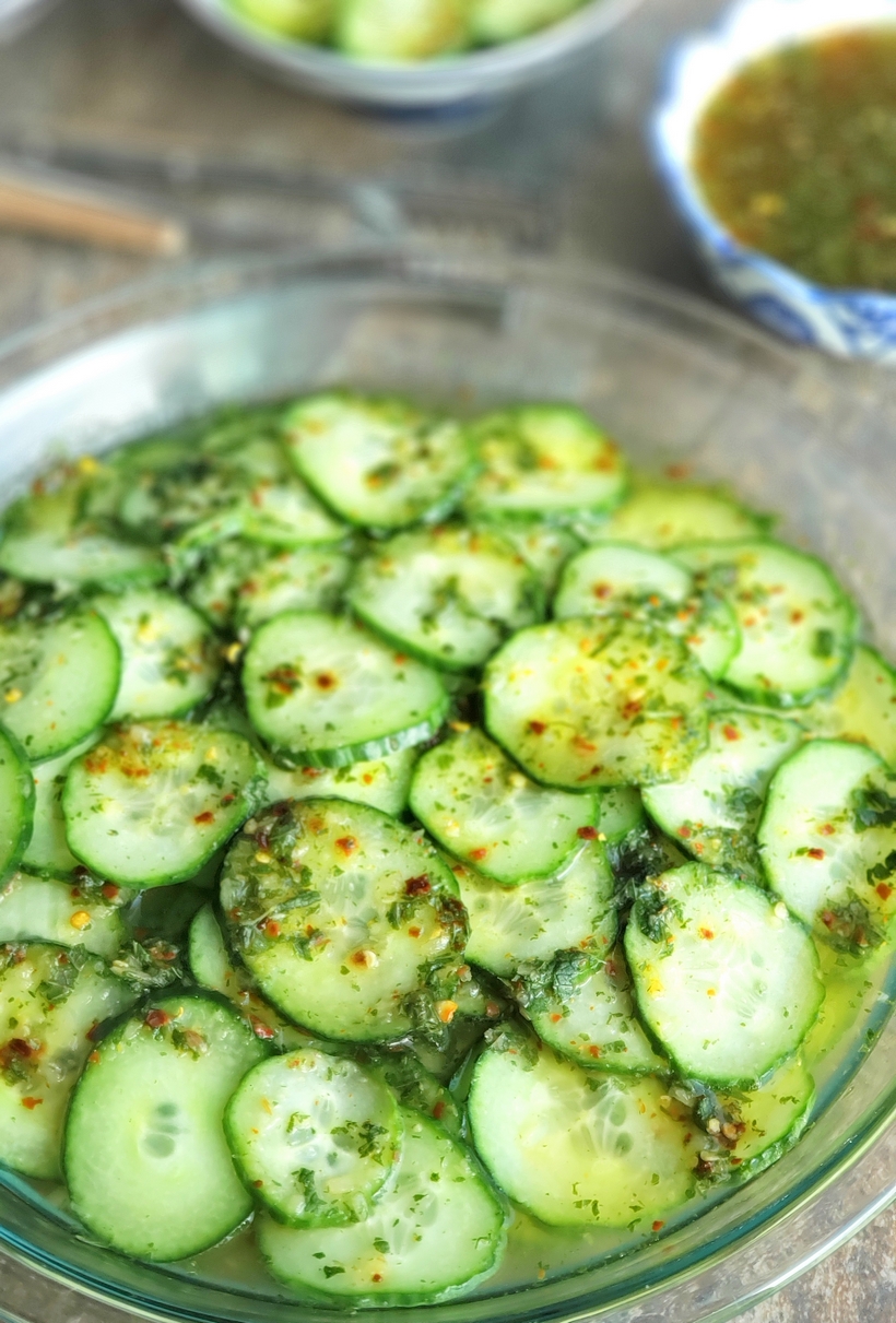 Sliced cucumbers in a large bowl with vinaigrette on top.