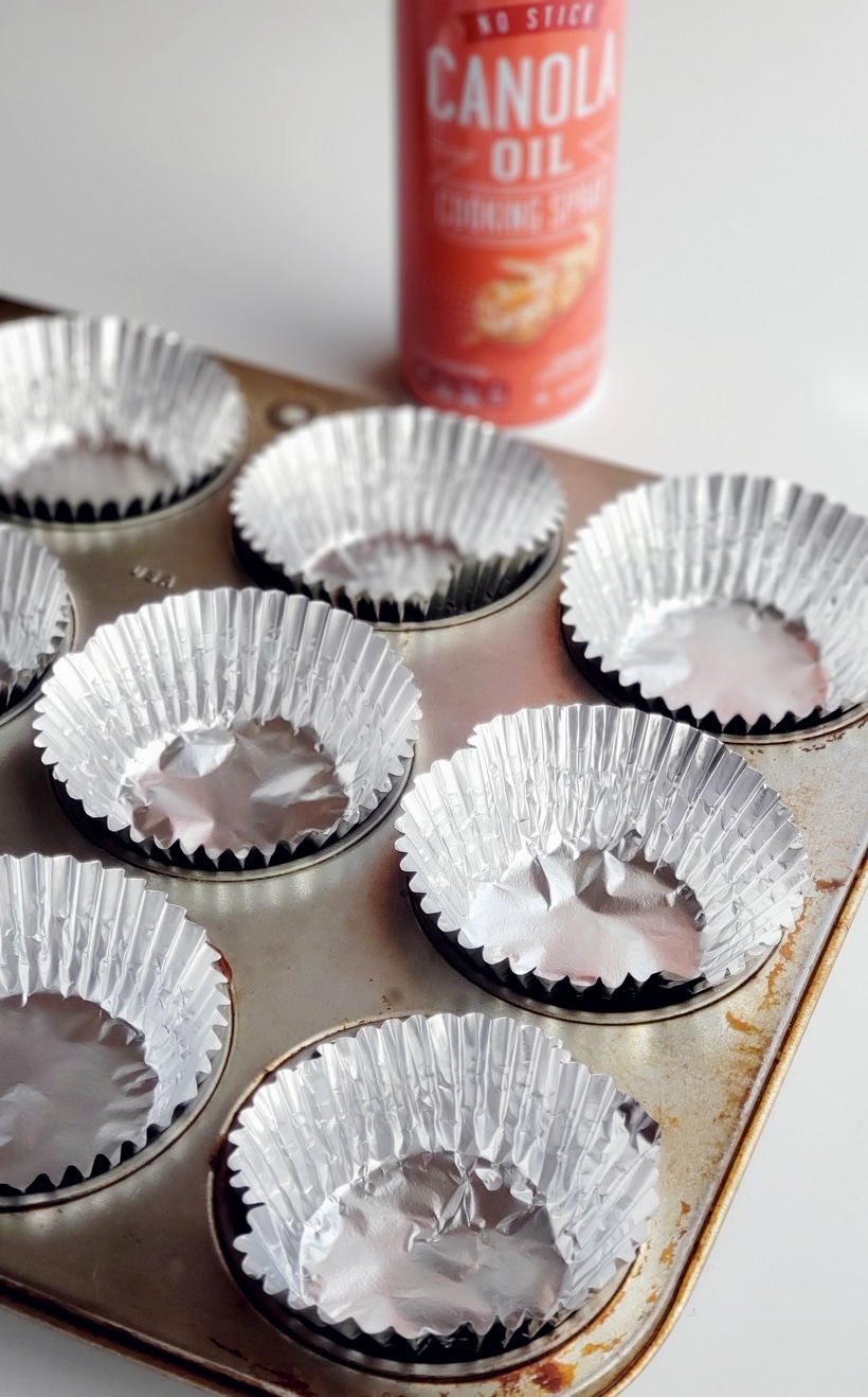Empty muffin liners in a muffin tin with cooking spray can.