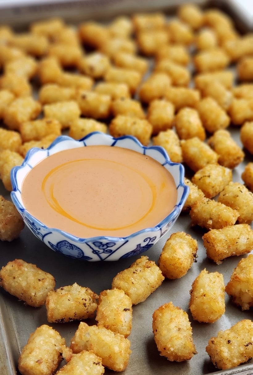Tater tots surrounding a bowl of sauce on a tray.
