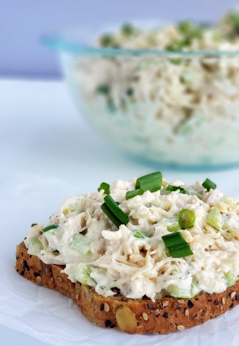 Chicken salad on a slice of bread with chicken salad in a bowl in the background.