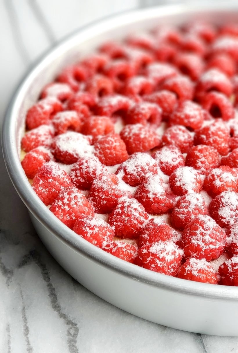 Raspberries on top of cake batter in a baking tin sprinkled with sugar.