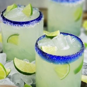 Three glasses with agave margaritas surrounded by ice and lime.