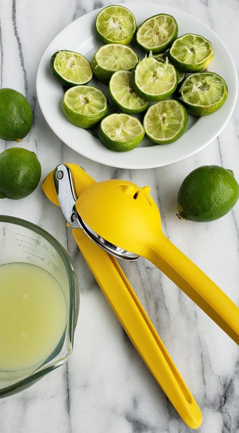 Lime juice, squeezed lime and citrus squeezing tool on white marble.