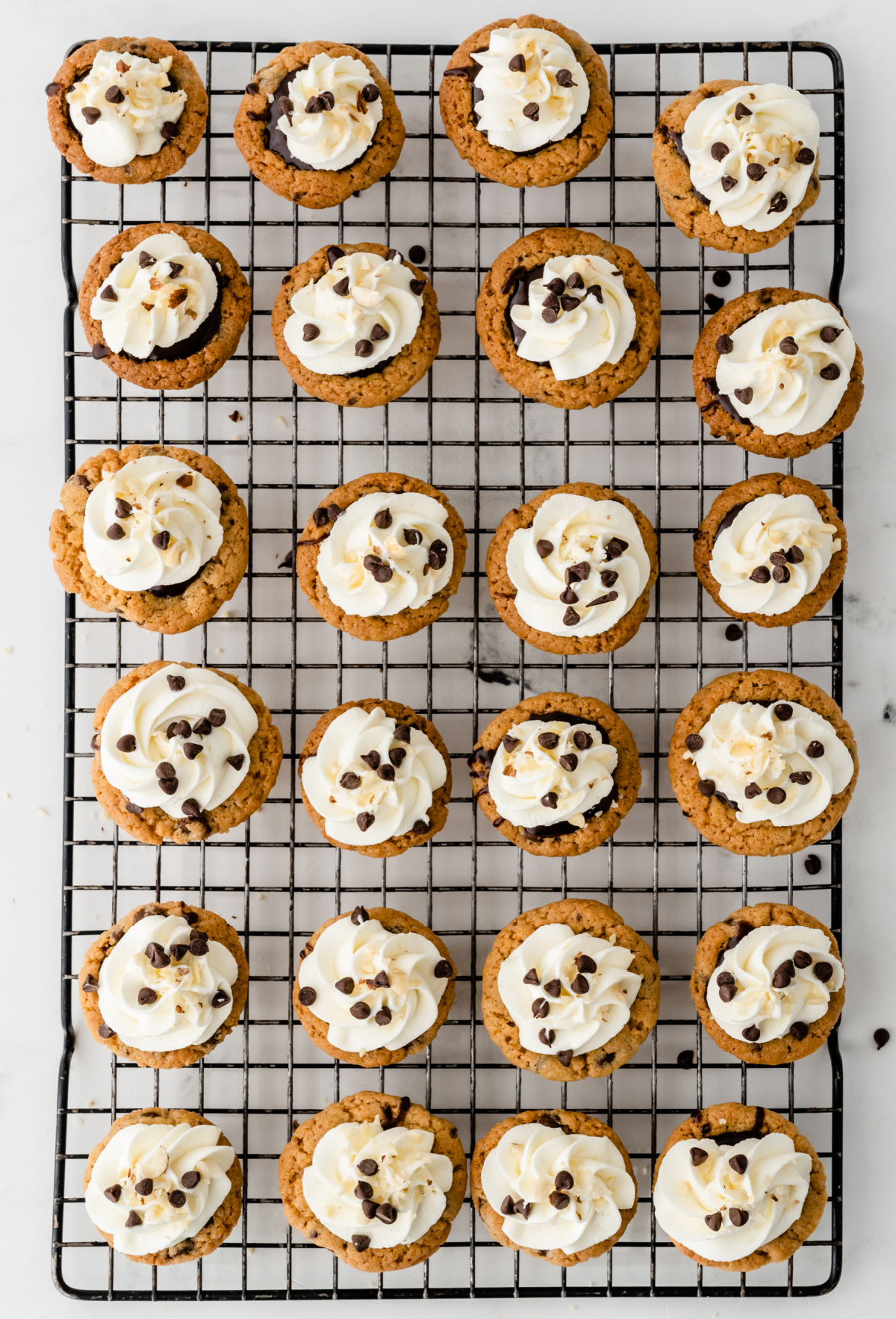 Chocolate chip cookie cups with Nutella filling and whipped cream arranged on a cooling rack