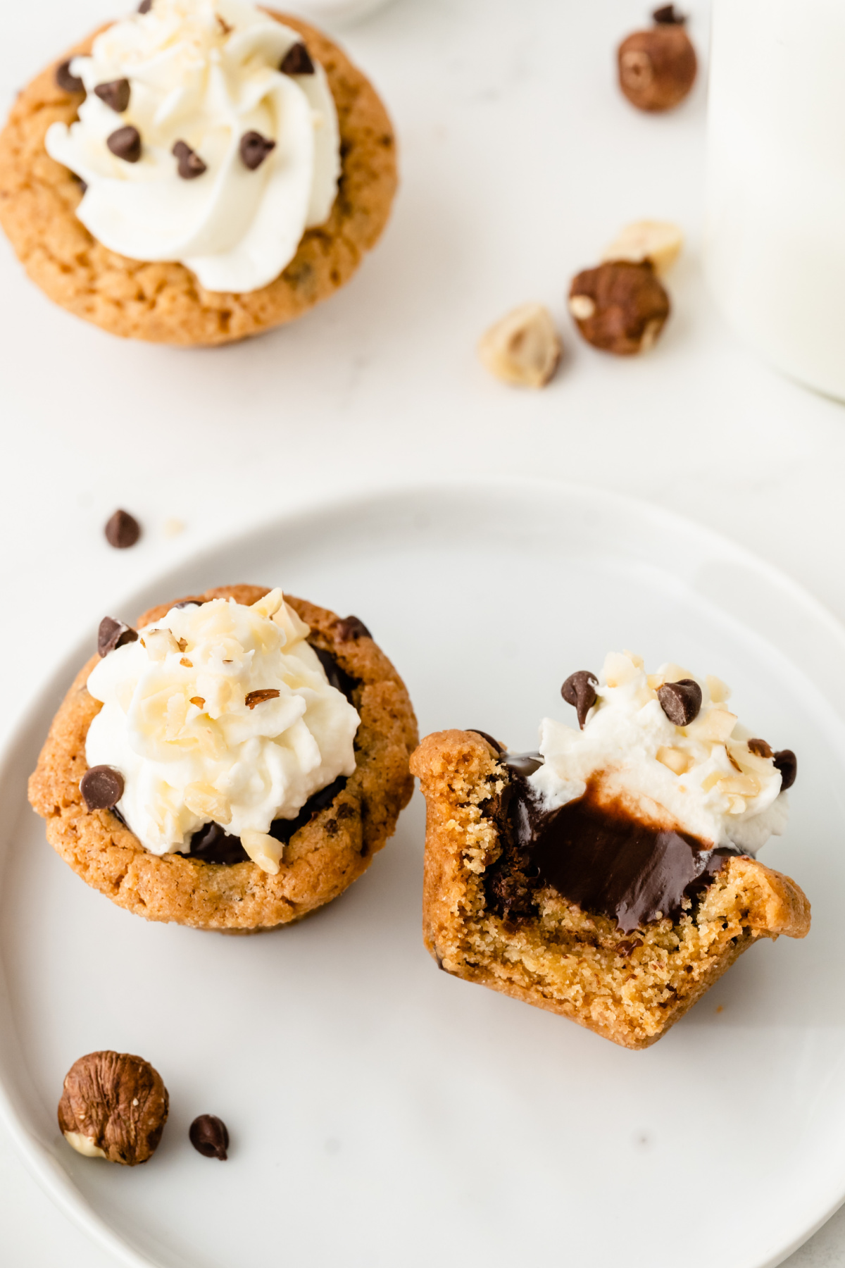 Chocolate chip cookie cup with Nutella center and whipped cream topping, one broken open to show filling