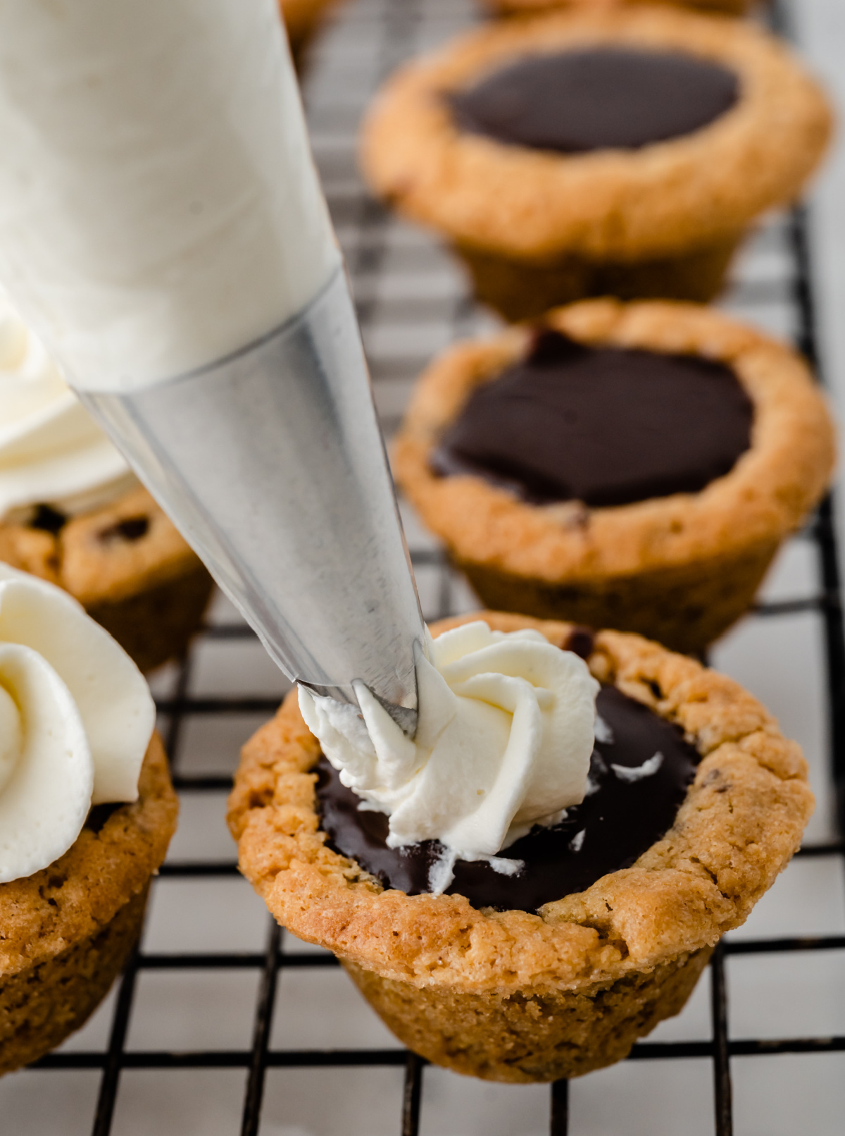 Nutella chocolate cookie cups being topped with whipped cream on a cooling rack