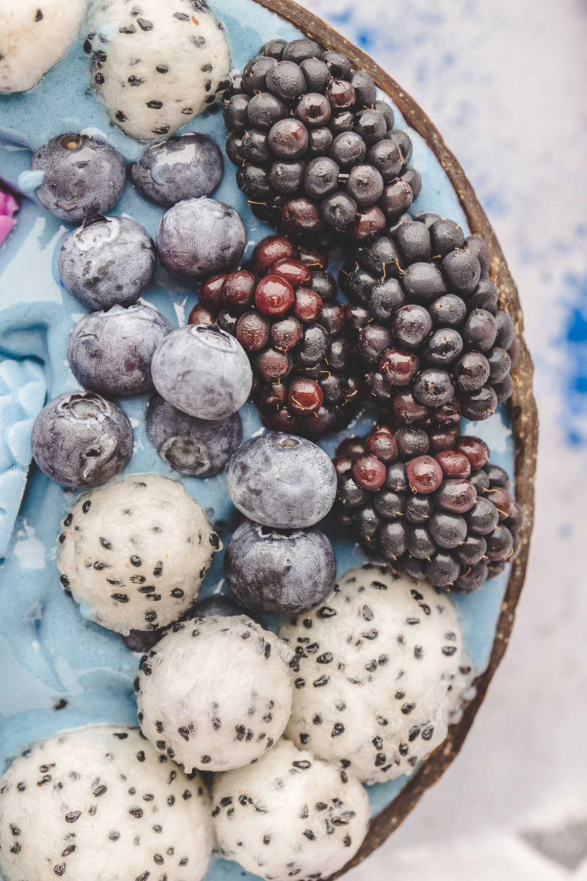 Close-up of dragon fruit, blueberries, and blackberries on top of a blue smoothie bowl.