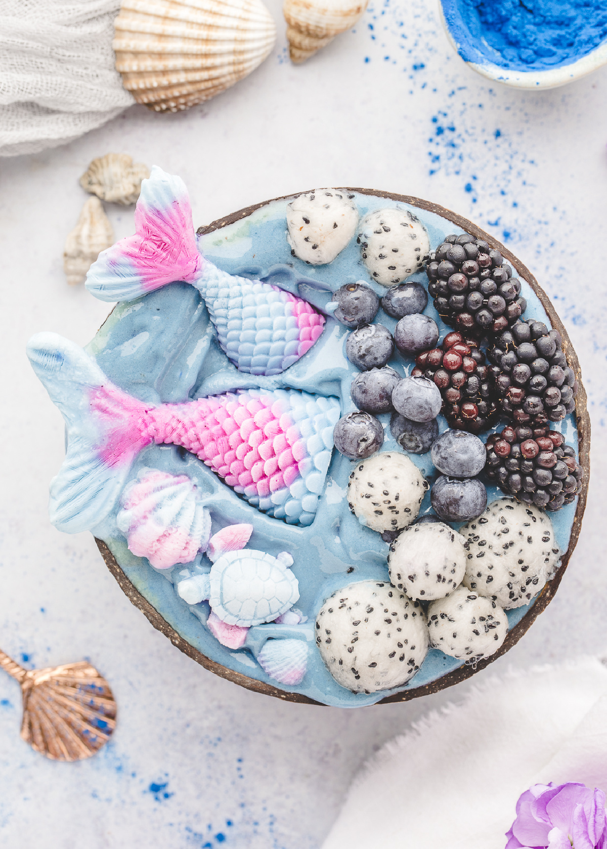 Mermaid smoothie bowls topped with yogurt mermaid tails, dragon fruit, blueberries, and blackberries in a coconut bowl.