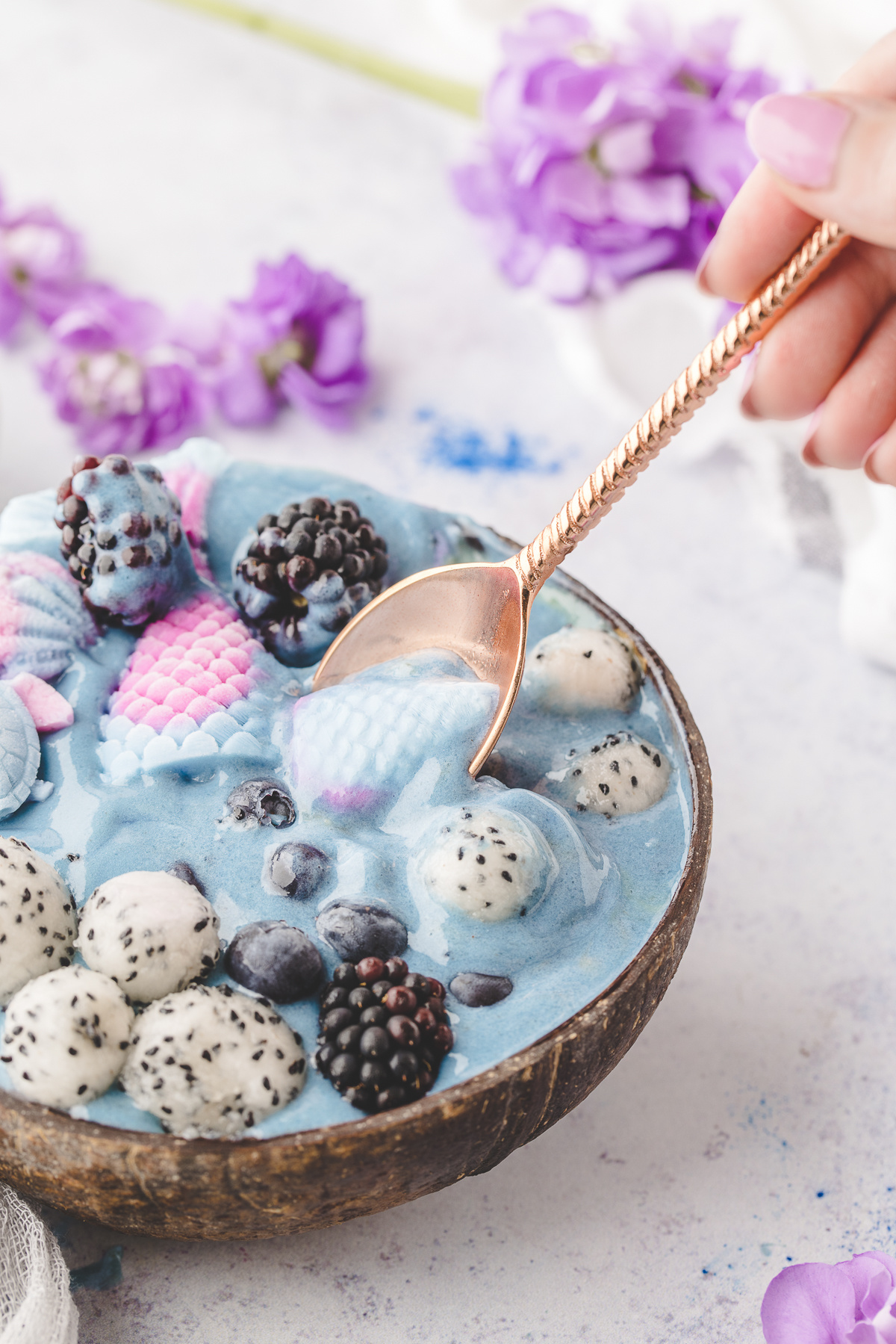 Spoon scooping a bite of a mermaid smoothie bowl with yogurt mermaid tails, dragon fruit, blueberries, and blackberries.