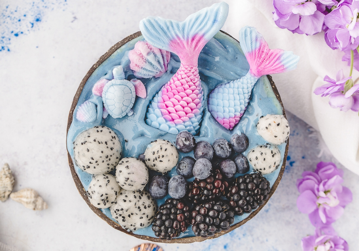 Overhead view of mermaid smoothie bowls topped with yogurt mermaid tails, dragon fruit, blueberries, and blackberries.