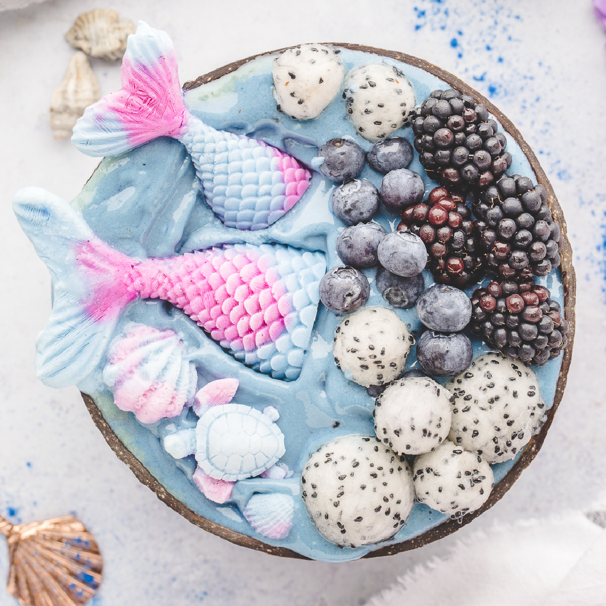 mermaid smoothie bowl topped with homemade yogurt mermaid tails, dragon fruit, blueberries, and blackberries.