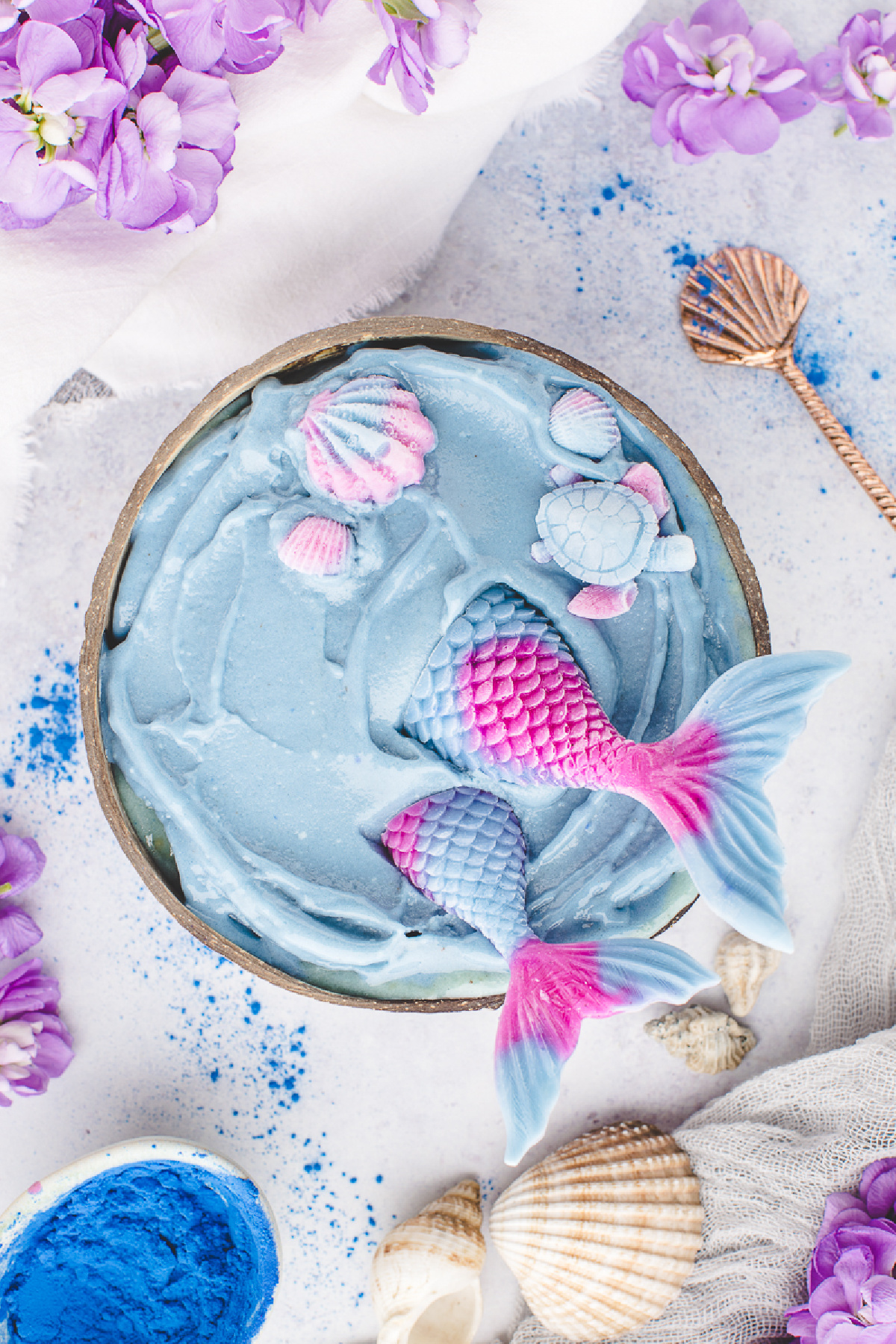 Blue smoothie base topped with homemade yogurt mermaid tails, seashells, and a turtle before adding fresh fruit.