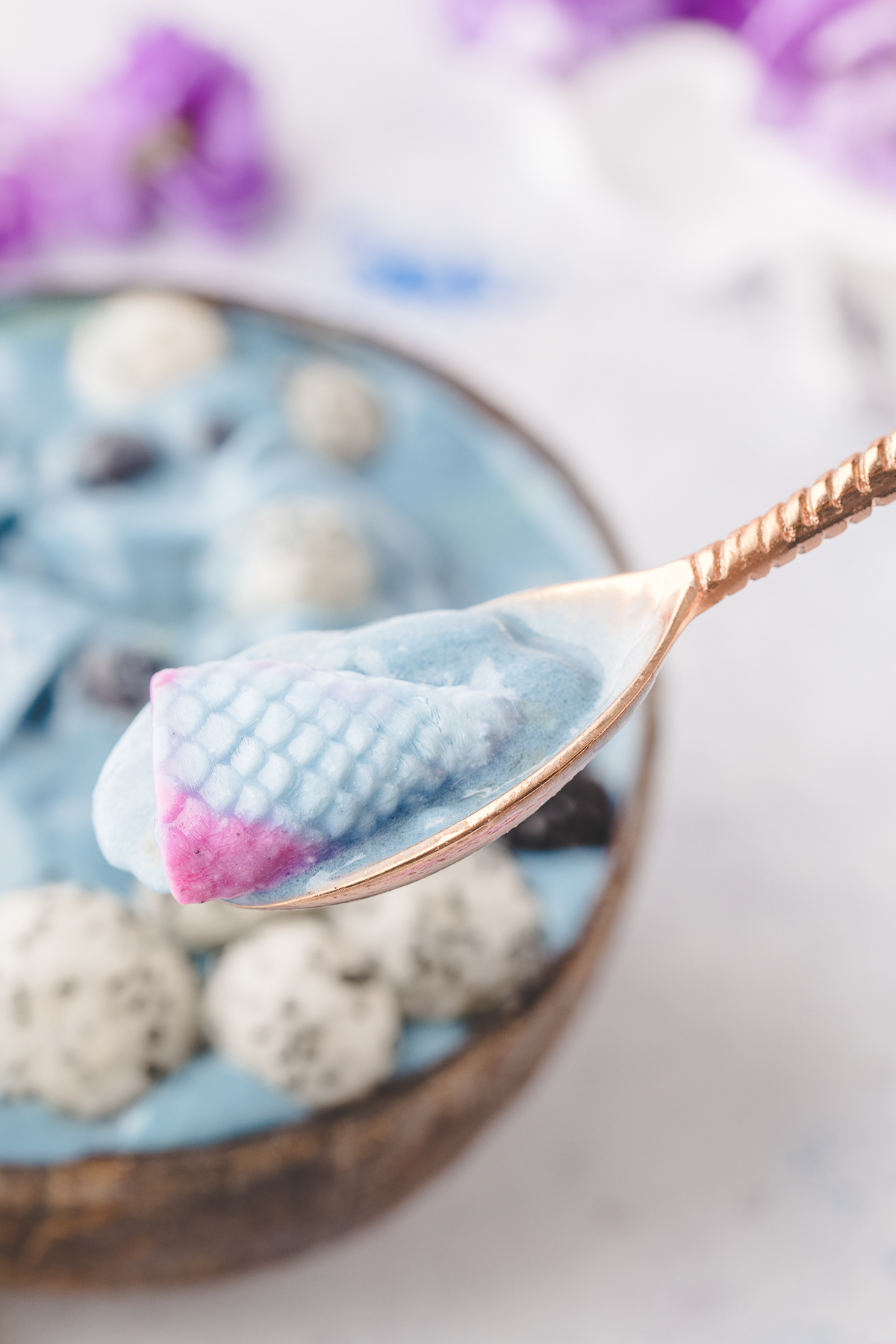 Close-up of a spoon holding a yogurt mermaid tail with a blue smoothie in the background.