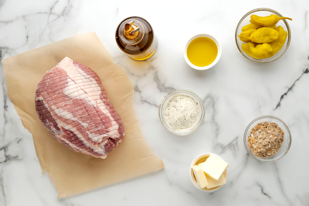 Ingredients for Mississippi Pork Roast Ingredients for slow cooker Mississippi pork roast including raw pork loin, ranch seasoning, onion soup mix, butter, olive oil, and pepperoncini.