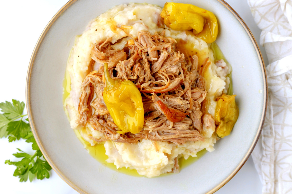 Shredded Mississippi Pork Loin with Pepperoncini Overhead view of shredded Mississippi pork loin served on mashed potatoes with yellow pepperoncini peppers and cooking liquid.