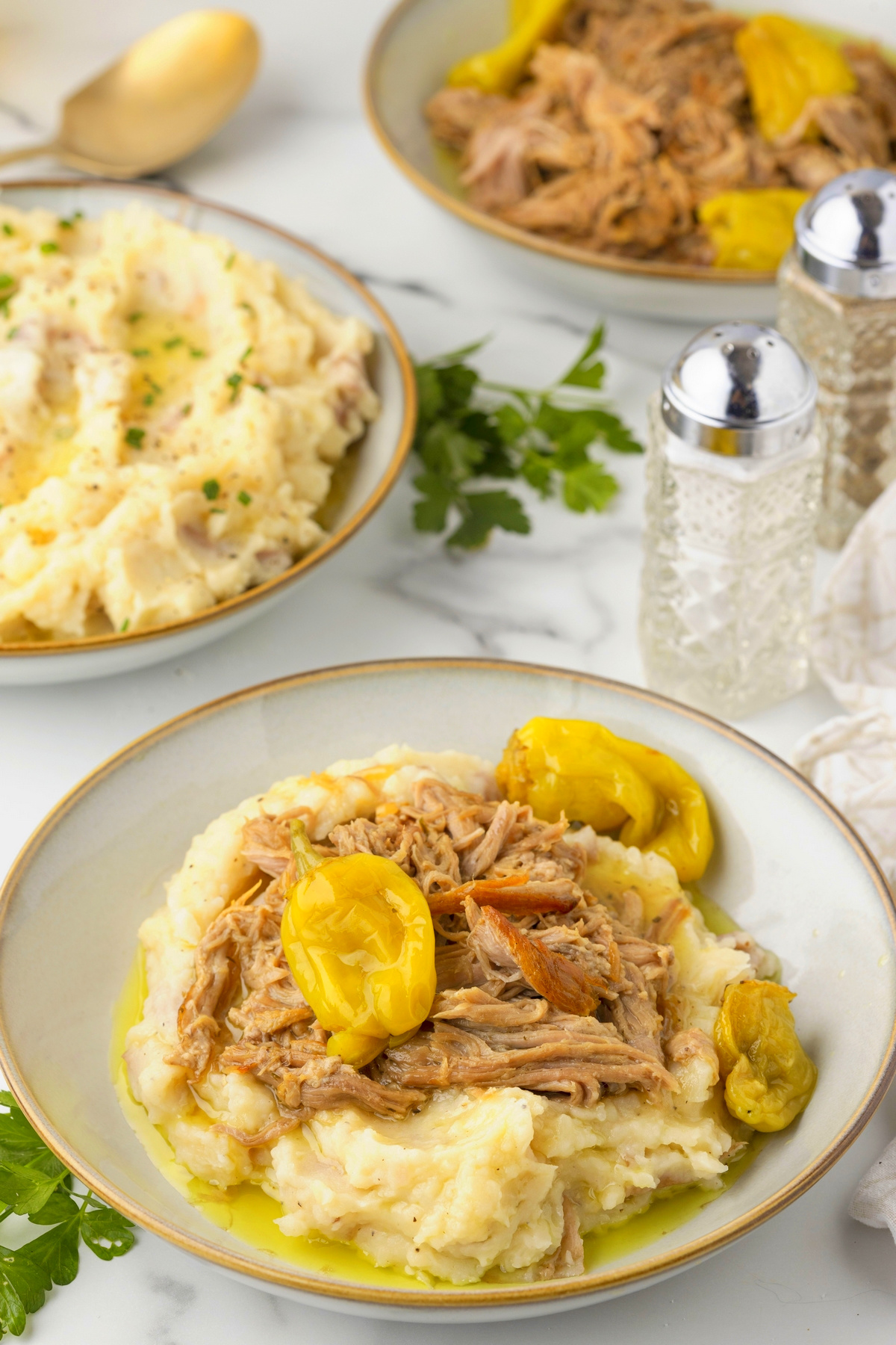 Slow Cooker Pork Roast Dinner with Mashed Potatoes Slow cooker Mississippi pork roast on mashed potatoes with pepperoncini peppers, with additional mashed potatoes and pork in the background.