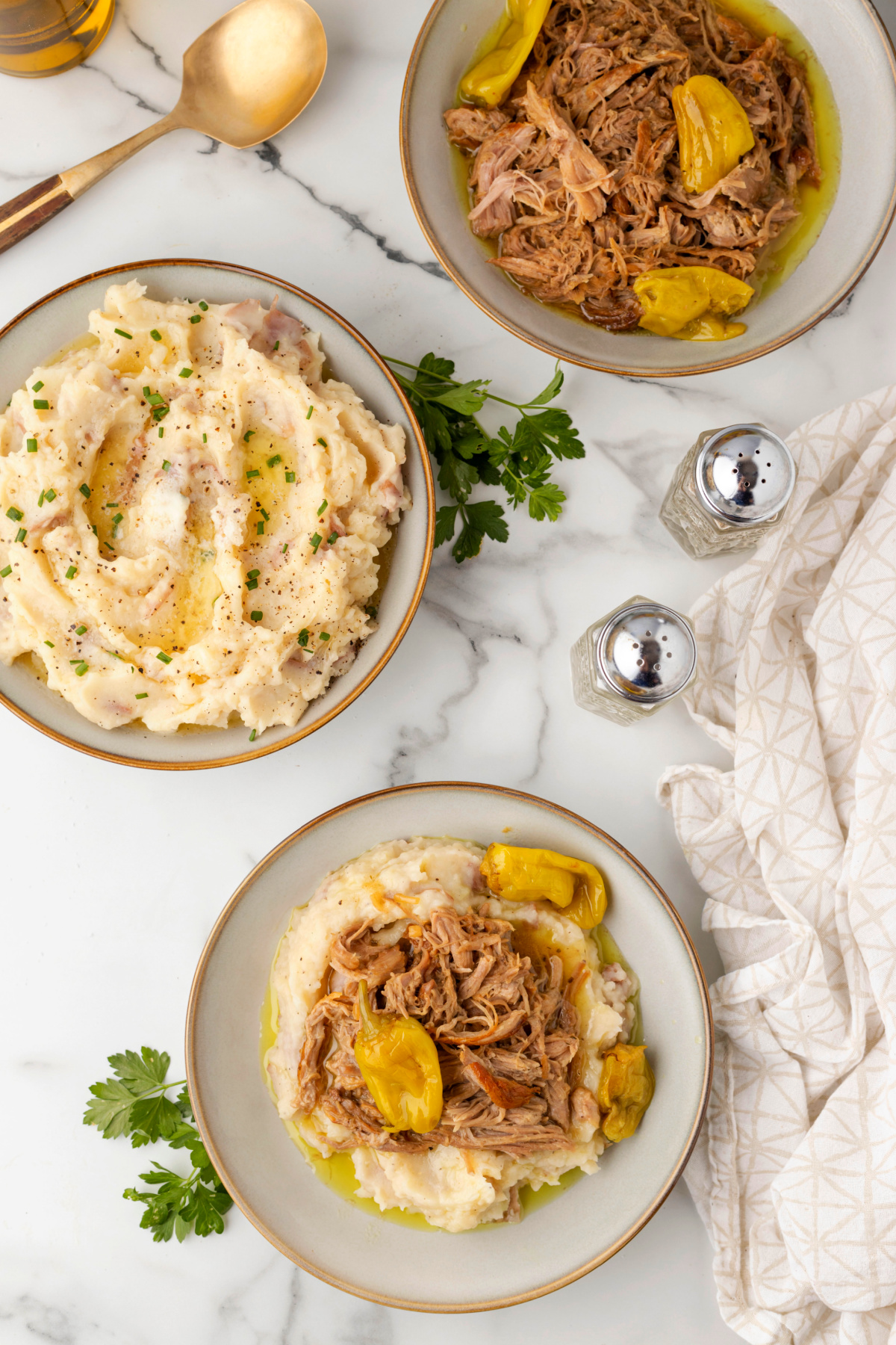 Mississippi Pork Roast Dinner Spread Overhead dinner spread of Mississippi pork roast over mashed potatoes, with separate bowls of shredded pork and mashed potatoes.