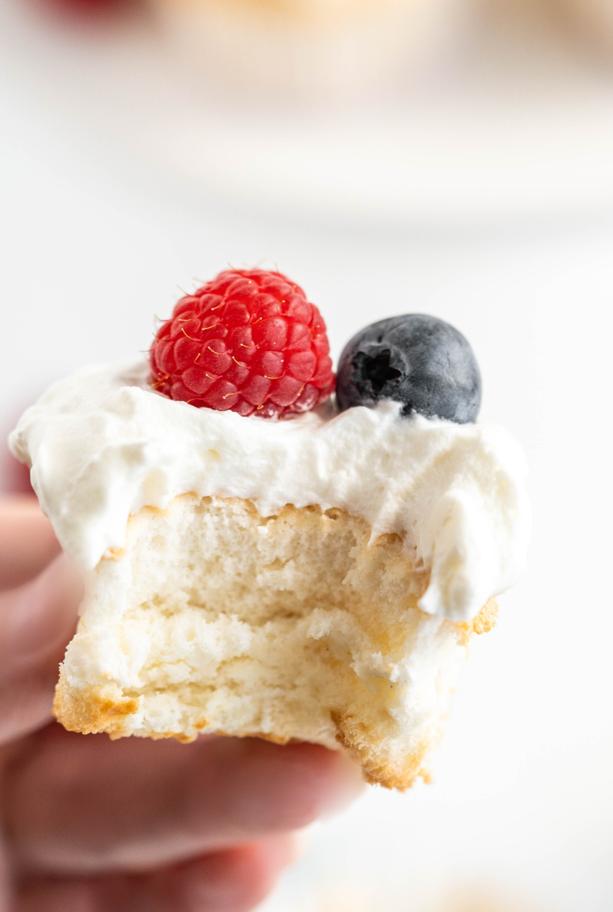 Bitten angel food cupcake showing its airy texture with whipped cream and fresh berries